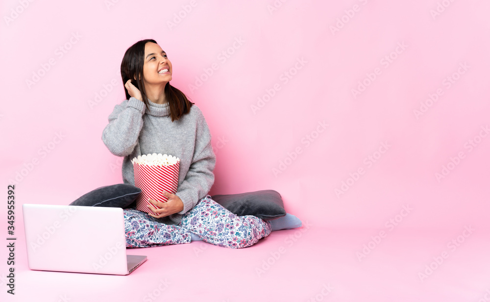 Young mixed race woman eating popcorn while watching a movie on the laptop thinking an idea Young mixed race woman eating popcorn while watching a movie on the laptop thinking an idea