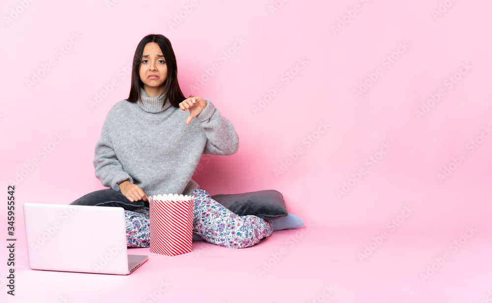 Young mixed race woman eating popcorn while watching a movie on the laptop showing thumb down with negative expression Young mixed race woman eating popcorn while watching a movie on the laptop showing thumb down with negative expression