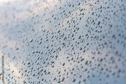 Shimmering raindrops on car surface. Reflected sky. Abstract background. Selective photo