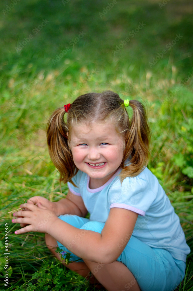 Cute little girl with bow tails sit and smile on the green meadow grass in summer day. happy international children's day. Cute little girl with bow tails sit and smile on the green meadow grass in summer day. happy international children's day.