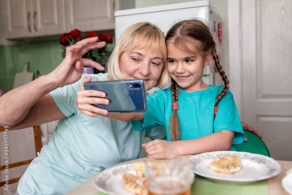 Happy grandchild teaching her grandma to use portative tablet and make selfie, new normal