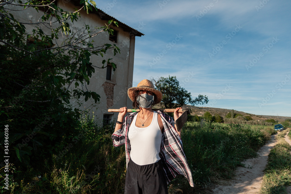 Young farmer woman walking with straw hat surgical mask and hoe