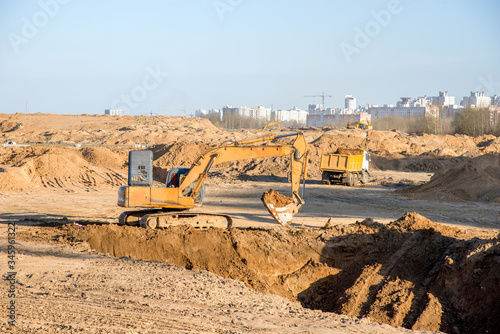 Large excavator working at construction site. Backhoe during earthworks on sand open-pit. Digging ground for the foundation and for laying sewer pipes district heating. Earth-moving heavy equipment