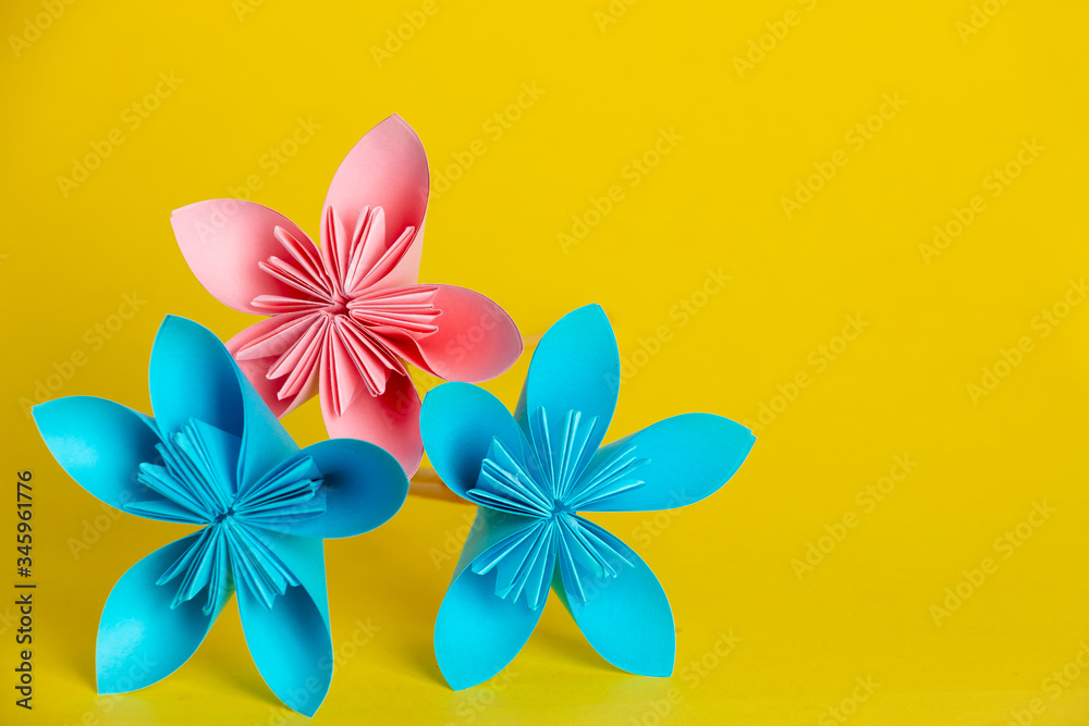 One pink and two blue flowers made of paper on a yellow background. DIY concept. Children's creativity.