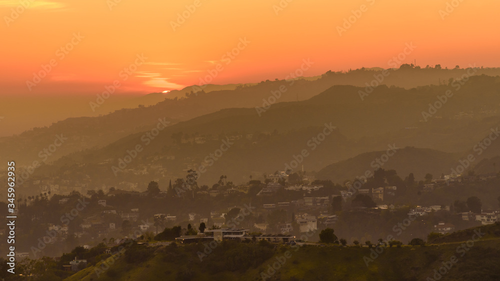 Sunset over the Hollywood Hills, Los Angeles. The sky is various shades of orange and yellow.