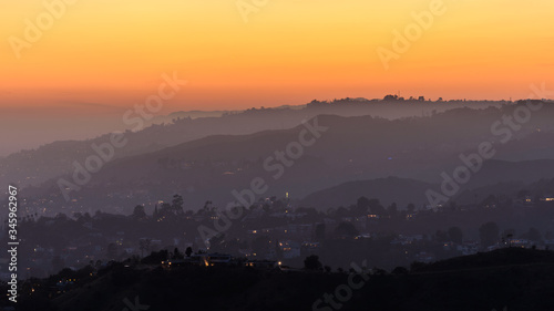 Sunset over the Hollywood Hills, Los Angeles. The sky is various shades of orange and yellow. © parkerspics