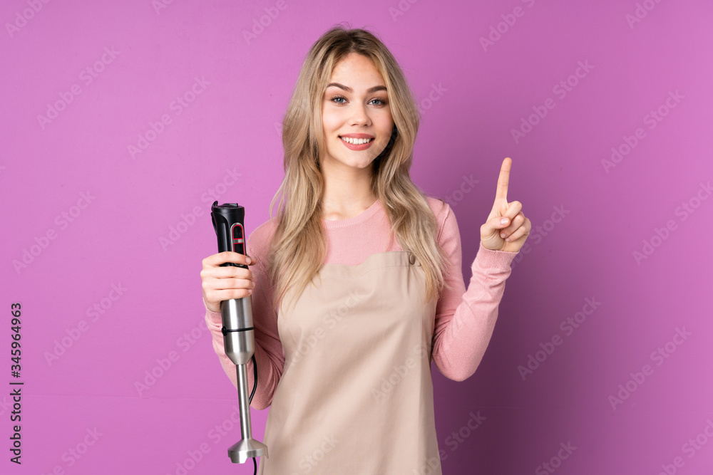 Teenager Russian girl using hand blender isolated on purple background showing and lifting a finger in sign of the best Teenager Russian girl using hand blender isolated on purple background showing and lifting a finger in sign of the best