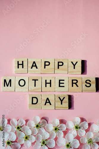 Happy Mother's day text on white spring flowers on pastel pink flat lay. Stylish floral greeting card. Happy mothers day. Spring snowflake, blooming flowers border
