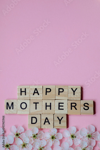 Happy Mother's day text on white spring flowers on pastel pink flat lay. Stylish floral greeting card. Happy mothers day. Spring snowflake, blooming flowers border