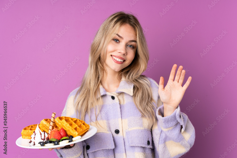 Teenager Russian girl holding waffles isolated on purple background saluting with hand with happy expression Teenager Russian girl holding waffles isolated on purple background saluting with hand with happy expression