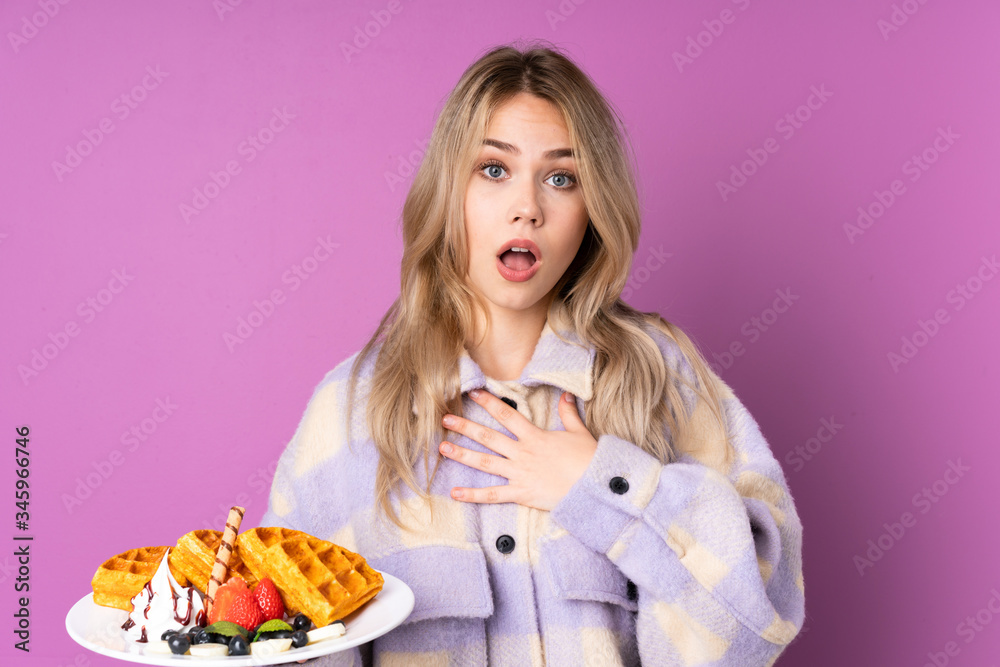 Teenager Russian girl holding waffles isolated on purple background surprised and shocked while looking right Teenager Russian girl holding waffles isolated on purple background surprised and shocked while looking right