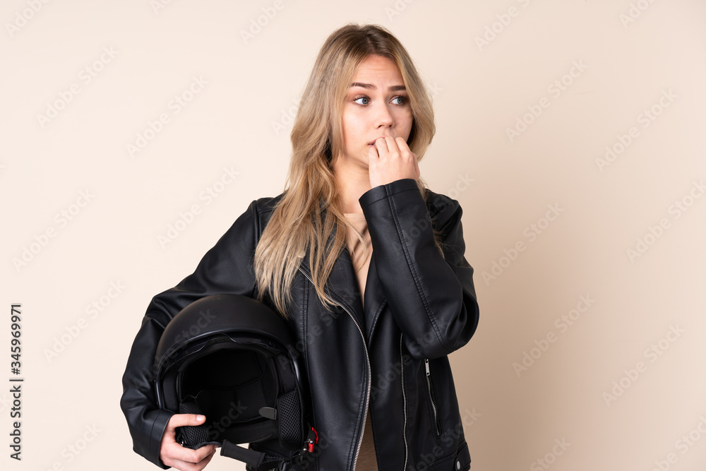 Russian girl with a motorcycle helmet isolated on beige background nervous and scared putting hands to mouth