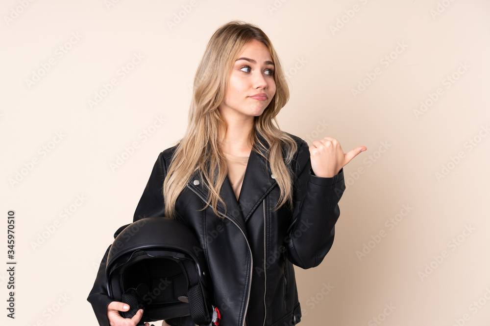 Russian girl with a motorcycle helmet isolated on beige background unhappy and pointing to the side Russian girl with a motorcycle helmet isolated on beige background unhappy and pointing to the side