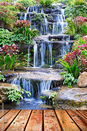 Fototapeta Naklejka Na Ścianę i Meble -  Wooden floor in front of the artificial waterfall and statue at the garden
