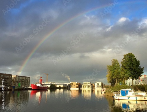 rainbow over cloudy sky above harbour with light house boat