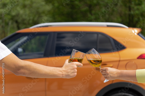 Fototapeta Naklejka Na Ścianę i Meble -  A couple celebrates buying a new car. Hands a man and a woman clink glasses against the background of the vehicle