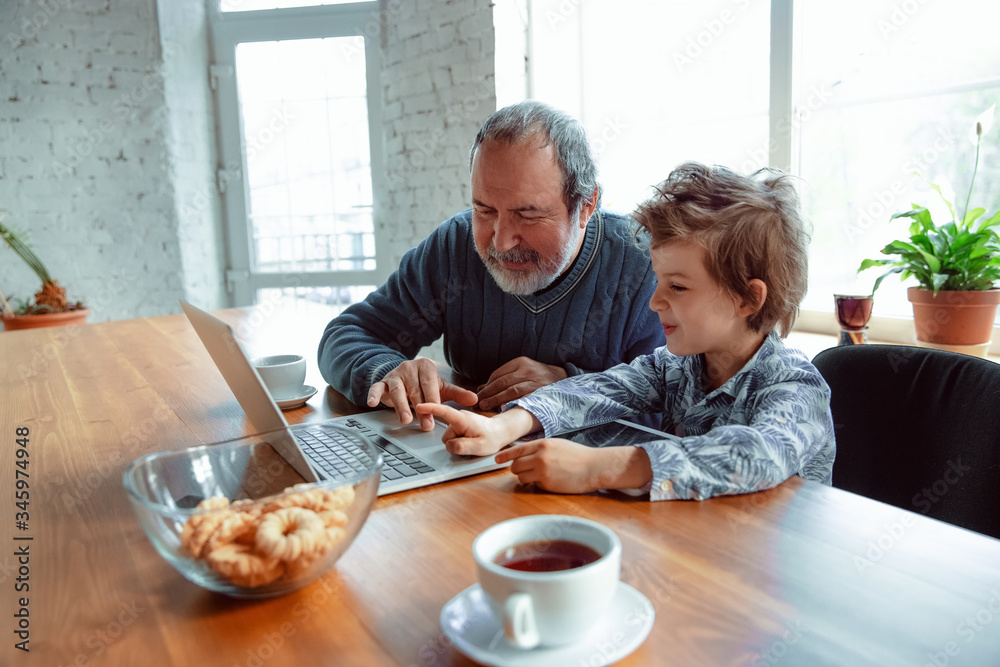 Using devices. Grandfather and his grandson spending time together insulated at home. Having fun, stadying online, reading and cleaning up. Concept of quarantine, family, love, realtions, togetherness Using devices. Grandfather and his grandson spending time together insulated at home. Having fun, stadying online, reading and cleaning up. Concept of quarantine, family, love, realtions, togetherness