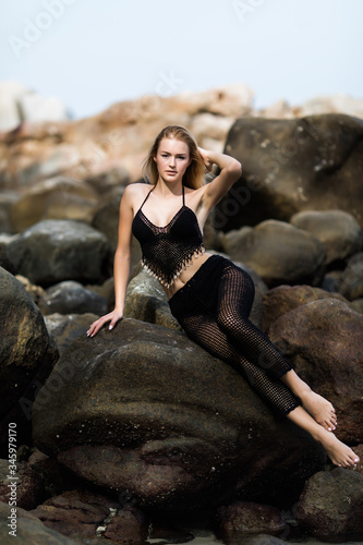 Young pretty woman in black bikini sitting on the cliff near Sea
