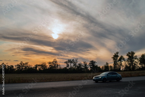 Sunset with bright fantastic clouds over the silhouette of trees behind the motorway.. © vladk213