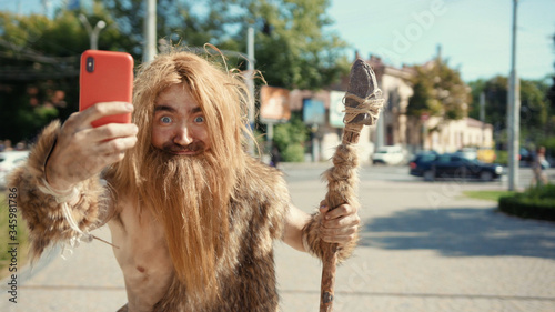 Φωτογραφία Prehistoric tribesman of neanderthals noticing somebody hurrying taking photographs like paparazzi on future smartphone in modern civilization city