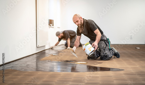 Zwei Handwerker   len den frisch geschliffenen Parkettboden