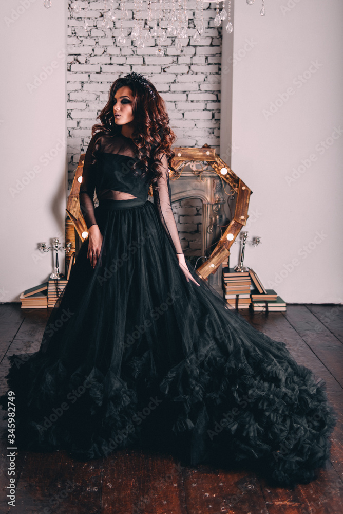 Naklejka premium a beautiful girl in a black dress with brown hair poses in a photo Studio
