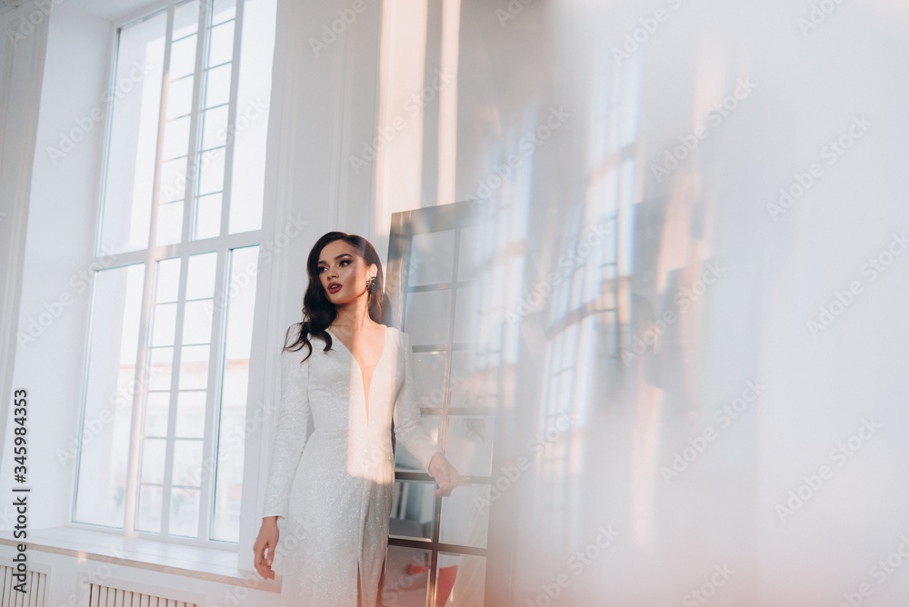 a beautiful bride in a white glittering wedding dress with brown hair poses in a photo Studio