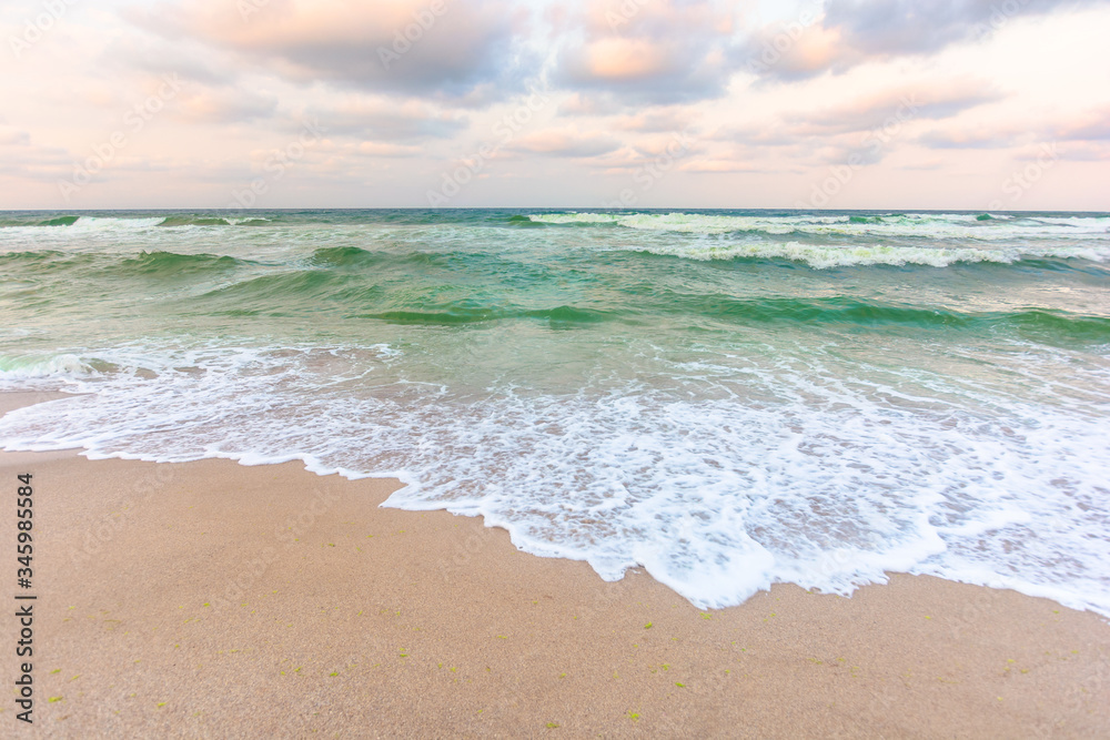 golden cloudy sunset above the green sea waters. waves crashing the sandy beach. clear horizon. changing windy weather