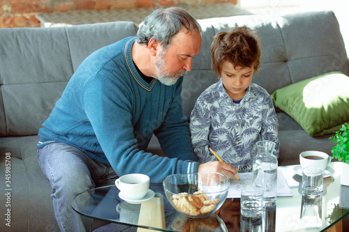 Useful time. Grandfather and his grandson spending time together insulated at home. Having fun, stadying, reading and drawing. Concept of quarantine, family, love, realtions, togetherness, education. photo