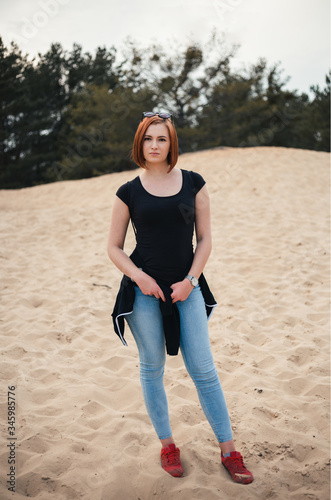 Portrait of beautiful and sexy brunette woman with pretty face and body on desert. Female model in blue jeans on the beach (sand) - vertical photot on sunset. photo