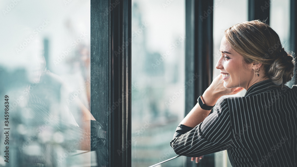 Portrait of sophisticated young successful confident CEO businesswoman looking out at the city from the office window.
