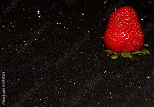 One strawberry on a black background with sequins. Red berry.