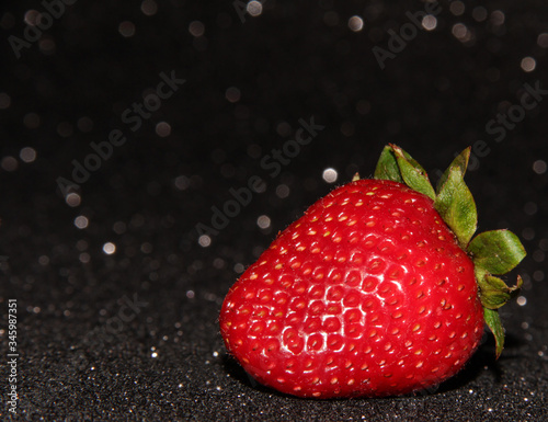One strawberry on a black background with sequins. Red berry.