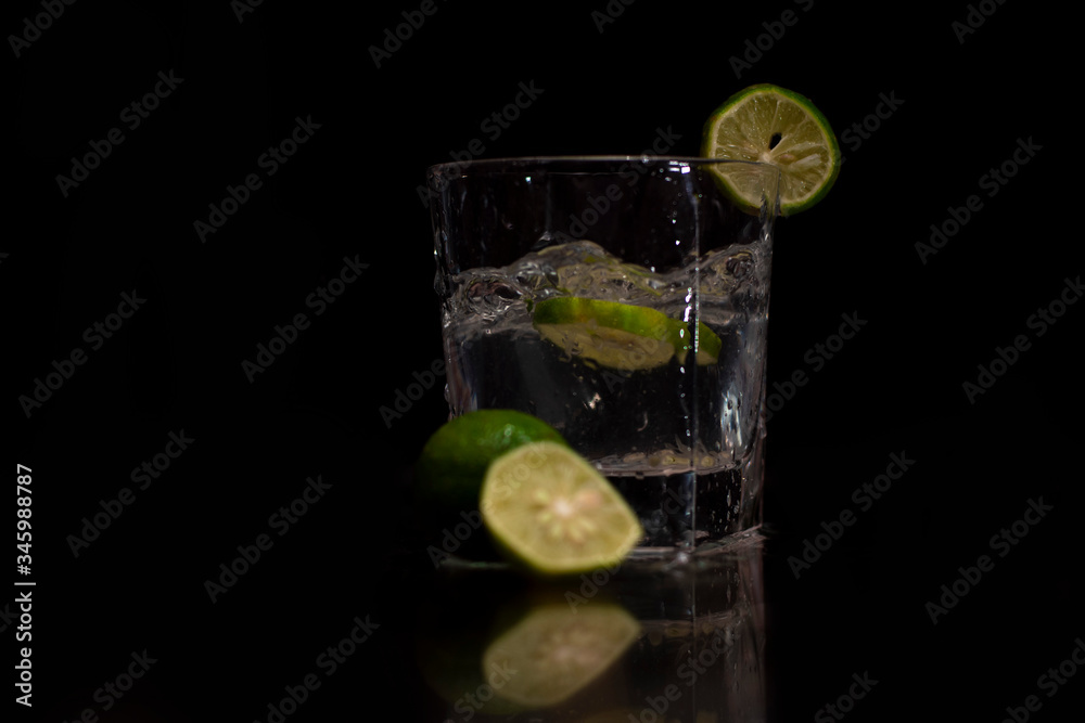 Water splashes out of the garnished glass as a green fresh lemon slice immerses into the water. Water splashes out of the garnished glass as a green fresh lemon slice immerses into the water.