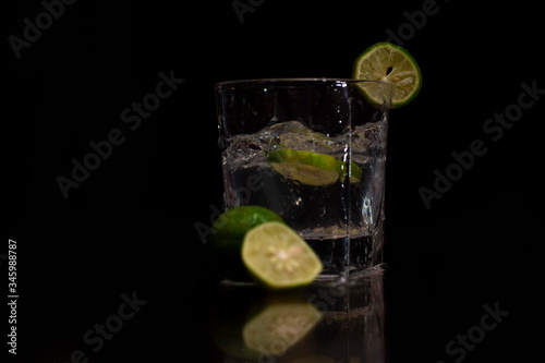 Water splashes out of the garnished glass as a green fresh lemon slice immerses into the water.