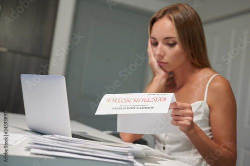 Worried young female with laptop reading eviction letter at home