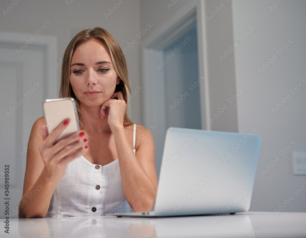 Young female sitting by computer and looking at the phone Young female sitting by computer and looking at the phone