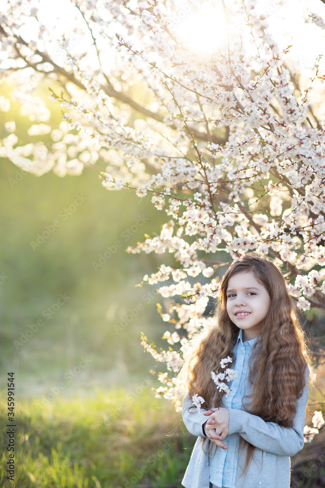 A little girl stands next to a flowering tree in nature A little girl stands next to a flowering tree in nature