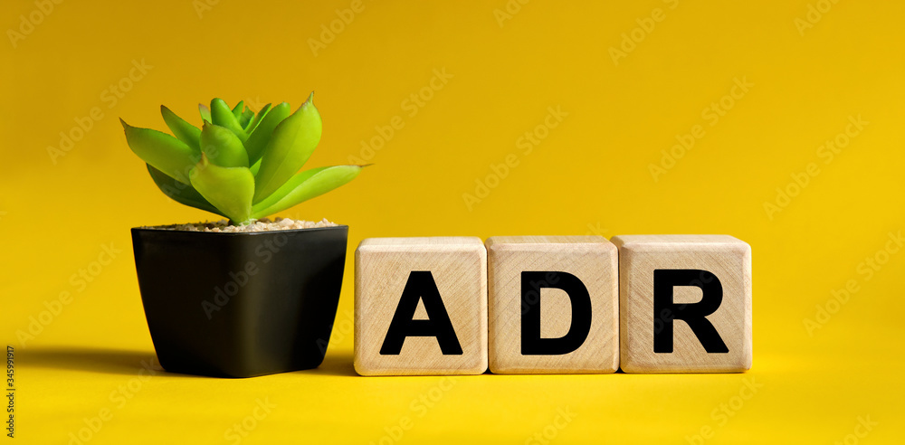 ADR - financial concept on a yellow background. Wooden cubes and flower in a pot. ADR - financial concept on a yellow background. Wooden cubes and flower in a pot.