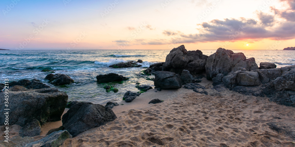 idyllic sunset on the sea shore. waves crashing rocks on sandy beach. beautiful cloudscape above the horizon