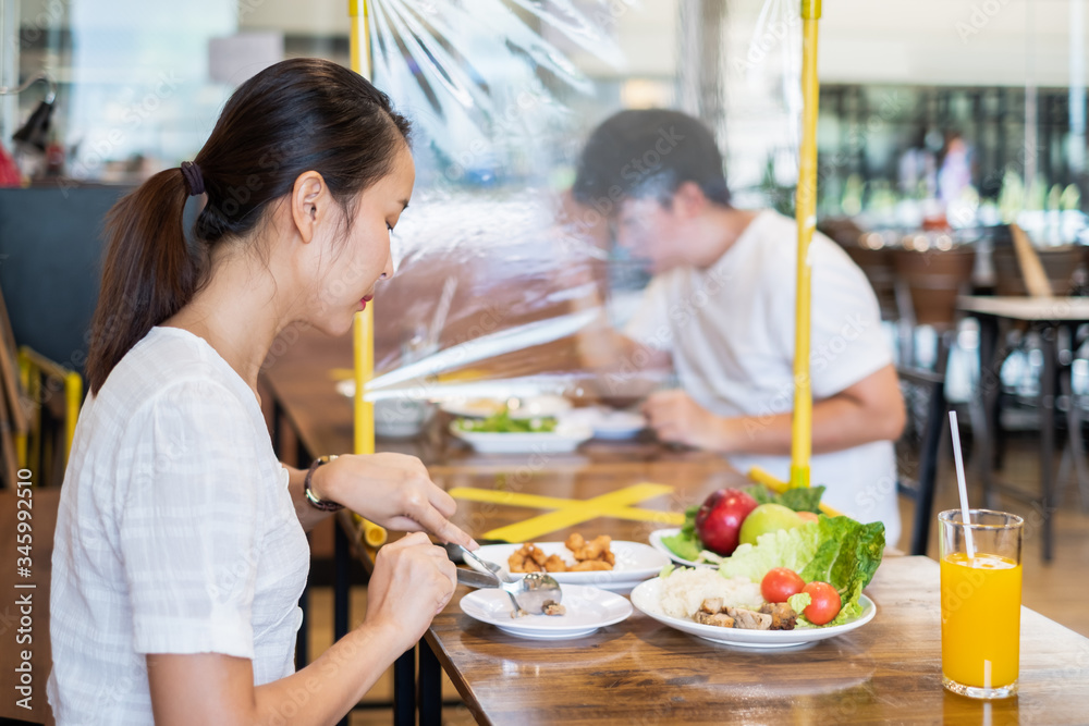 Asian couple man and woman sitting in restaurant eating food with table shield to protect infection from coronavirus covid-19, restaurant and social distancing concept Asian couple man and woman sitting in restaurant eating food with table shield to protect infection from coronavirus covid-19, restaurant and social distancing concept