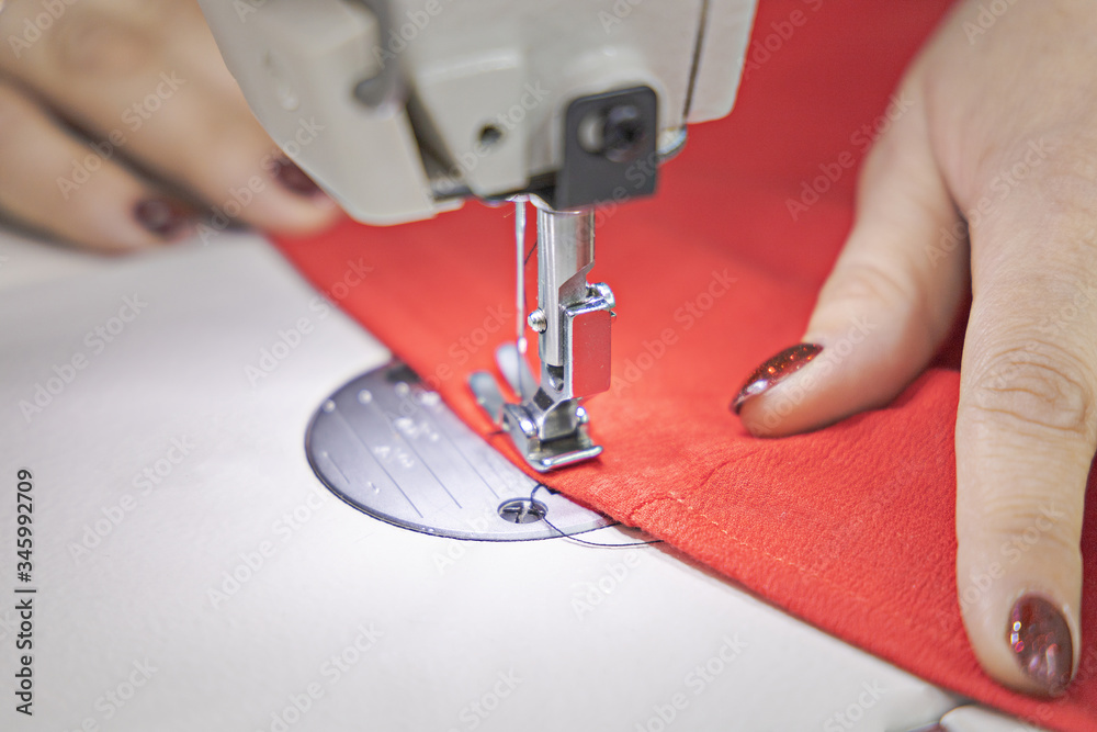 The master sews on a sewing machine. The master is sewing red fabric on a sewing machine. Closeup