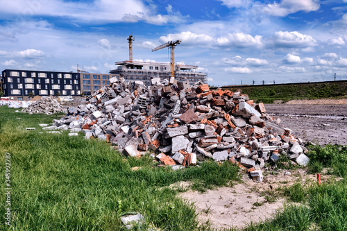 Construction site with cranes under blue skies, in the foreground a pile of rubble