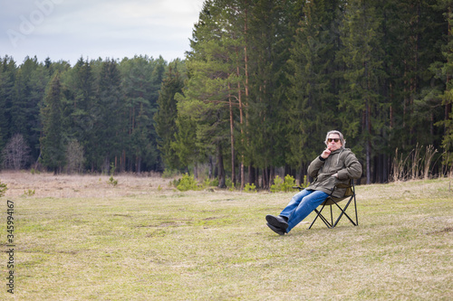 Adult man enjoying the nature while sitting in a camp chair in the early spring. The concept of a healthy lifestyle for older people. © papa