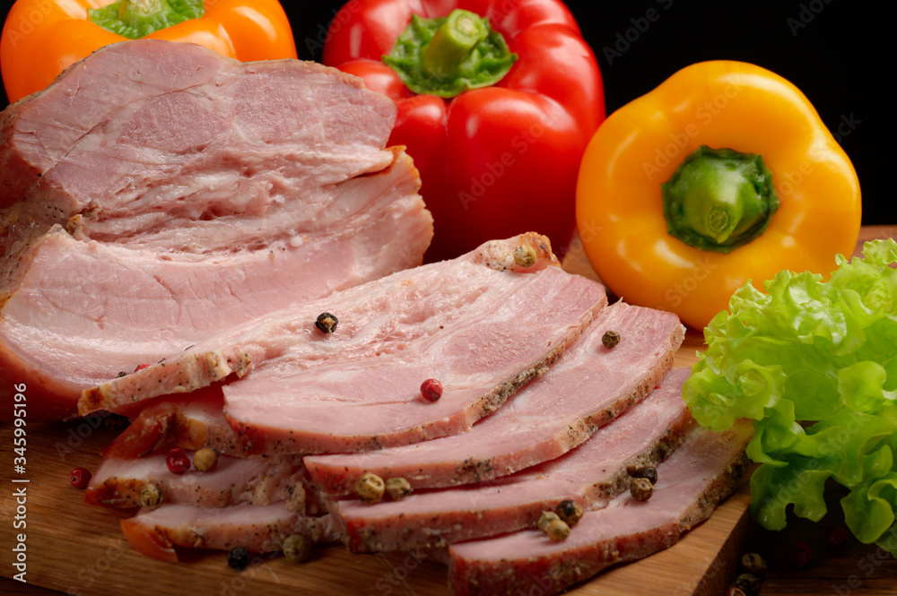 Smoked meat with spices cut into slices, with sweet peppers and herbs, on a cutting Board with a black background. eco-friendly ingredients for making a delicious and healthy snack.