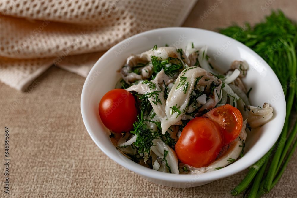 Marinated oyster mushrooms, garnished with cherry tomatoes and green dill. A dish with onions and butter in a white plate with a beige light cloth on the table Marinated oyster mushrooms, garnished with cherry tomatoes and green dill. A dish with onions and butter in a white plate with a beige light cloth on the table