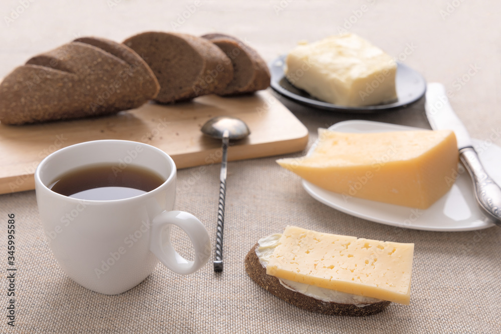 Sliced bread and knife on a cutting board. Butter, cheese, a cup of coffee on a sackcloth. Side view breakfast brunch on table concept