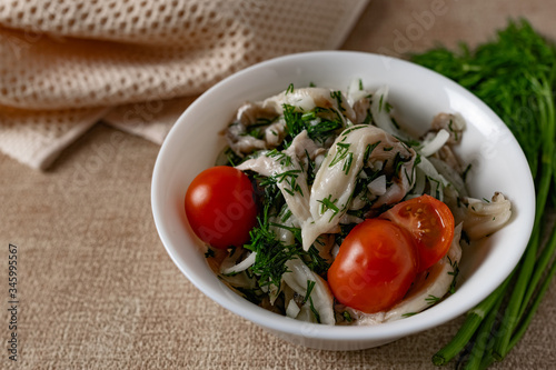 Marinated oyster mushrooms, garnished with cherry tomatoes and green dill. A dish with onions and butter in a white plate with a beige light cloth on the table