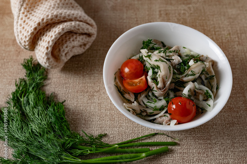 Marinated oyster mushrooms  garnished with cherry tomatoes and green dill. A dish with onions and butter in a white plate with a beige light cloth on the table