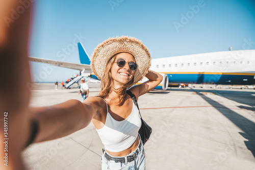 Beautiful happy woman taking a selfie at the airport in front of the plane. People departure boarding holidays concept.  photo